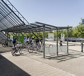 Fahrradüberdachung PEGASUS mit Trogdach, Dachbreite x Dachtiefe 9300 mm x 4500 mm, Seitenwände (Siebdruck nach Kundenvorgabe gegen Mehrpreis), Schließfachanlage SECURE, Fahrradparkern BERN, Stahlkonstruktion in RAL 9002 perldunkelgrau