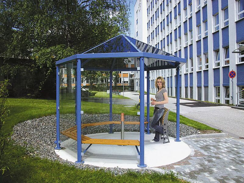 raucherunterstand-aqua__shoKAT0007689 Einzel-Pavillon AQUA, mit 5 Holzsitzbänken, Anlehnstütze RELIEF und Ascher CYCAS, Dacheindeckung VSG bronce getönt (auftragsbezogene Anpassung), 6 Seitenwandscheiben ESG Klarglas, Stahlkonstruktion in RAL 5015 himmelblau