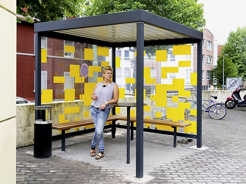 raucherunterstand-tobacco__shoKAT0055481 Raucherunterstand TOBACCO, Dachbreite x Dachtiefe 2400 mm x 2400 mm, mit Rück- / 1 Seitenwand, zweiseitige Sitzbank TOBACCO, Abfallbehälter / Ascher CALGARY sowie Stehtisch BISTROT, Stahlkonstruktion in RAL 7016 anthrazitgrau, Scheibendekorbeklebung ba...