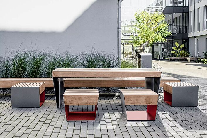 Sitz BLOCQ mit Jatobaholzbelattung, Stahlteile in bicolour (Sonderausführung in RAL 9007 graualuminium und RAL 3020 verkehrsrot), Sitzbank BLOCQ, Tisch BLOCQ (Sonderausführung) und Abfallbehälter PRAX