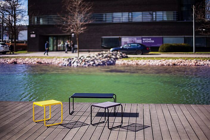 Sitz STACK ohne Rückenlehne, in RAL 1021 rapsgelb und RAL 9005 tiefschwarz sowie Tisch STACK mit HPL-Auflage in Black 0080, Stahlteile in RAL 9005 tiefschwarz