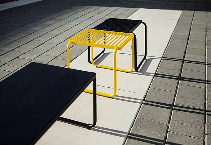 Sitz STACK ohne Rückenlehne, in RAL 1021 rapsgelb und RAL 9005 tiefschwarz sowie Tisch STACK mit HPL-Auflage in Black 0080, Stahlteile in RAL 9005 tiefschwarz
