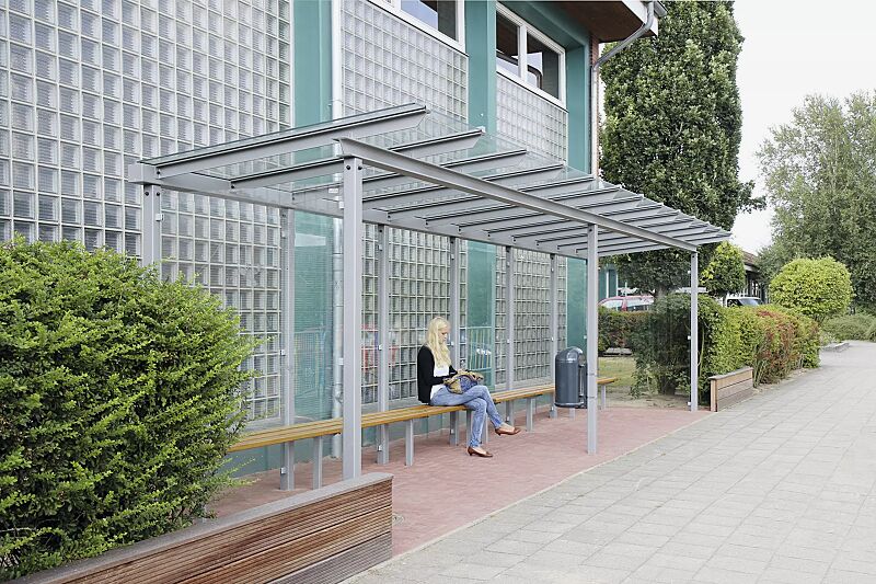 wartehalle-pegasus__shoKAT0029885 Wartehalle PEGASUS, Dachbreite x Dachtiefe 9300 mm x 2000 mm, mit Rück- / Seitenwände ESG, Klarglas sowie Sitzbank FERMO und Abfallbehälter DERBY, Stahlkonstruktion in RAL 9006 weißaluminium