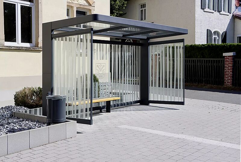 Wartehalle PURE, Dachbreite x Dachtiefe 4000 mm x 1800 mm, Rück- / Seitenwände ESG, Klarglas mit bauseitiger Folierung, Sitzbank PURE, Abfallbehälter KÖLN, Stahlkonstruktion in RAL 7016 anthrazitgrau