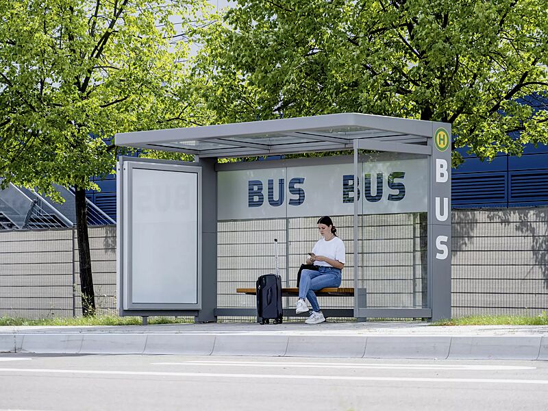 Wartehalle PURE, Dachbreite x Dachtiefe 4000 mm x 1800 mm, Rück- / Seitenwände ESG, Klarglas mit bauseitiger Folierung, Werbevitrine CITY-LIGHT, Sitzbank PURE, Stahlkonstruktion in RAL 7037 staubgrau